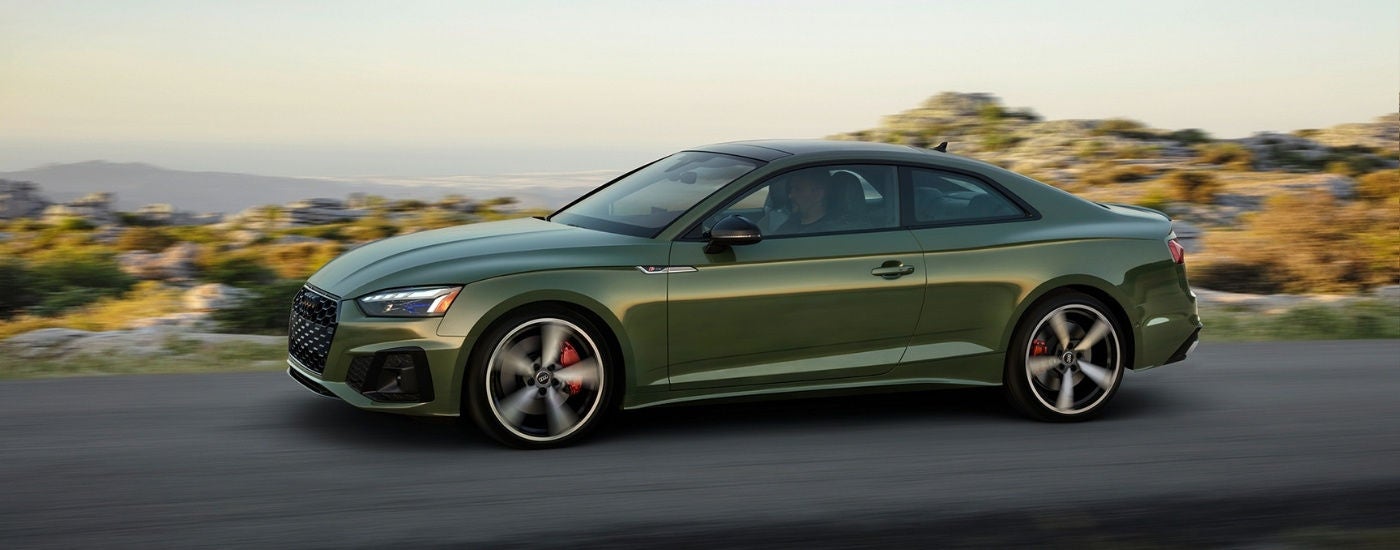 Side view of green 2025 Audi A5 Coupe driving on a road.